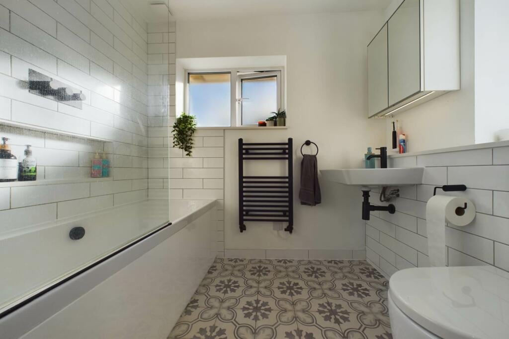 Bright renovated bathroom with white wall tiles, patterned floor and black towel radiator